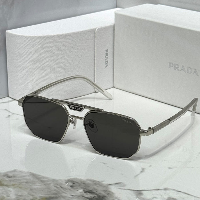 Prada sunglasses with dark lenses and silver-tone metal frames, displayed in front of white Prada boxes on a light marble-like surface.