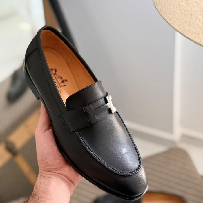 Black loafer shoe held in a hand with a blurred background